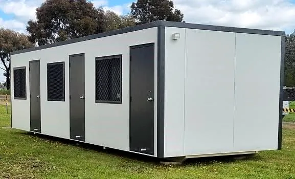 White portable building with charcoal frame, several doors and security-screened windows, on grass.